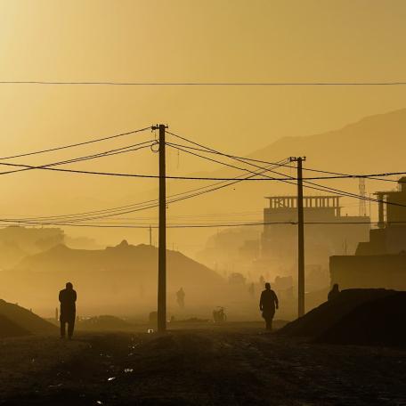 Dusk in Kabul, Afghanistan. Telephone poles and a few pedestrians are in the foreground with mountains in the background.