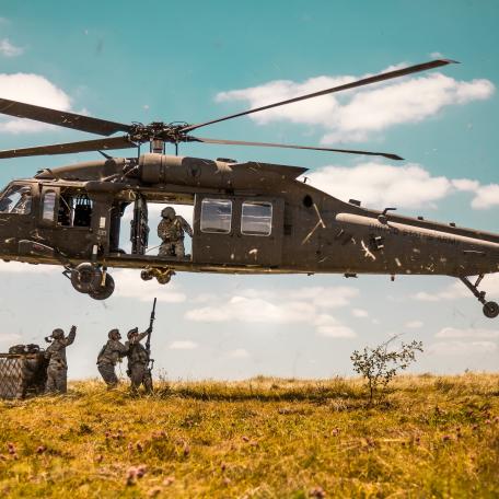 Helicopter hovering over military personnel.